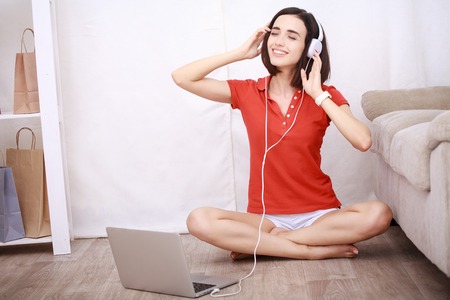Smiling young woman in headphones sitting on floor at home using laptop and listening music, technology and communication conceptの写真素材