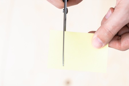 A man is cutting a sheet of yellow paper using metallic scissorsの写真素材