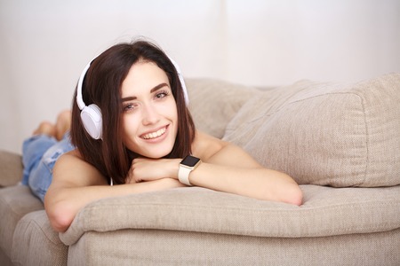 Woman listening music in headphones sitting on sofa in roomの写真素材
