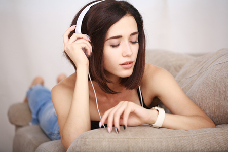 Woman listening music in headphones sitting on sofa in roomの写真素材