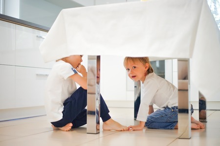 Two happy children playing under table in kitchenの写真素材