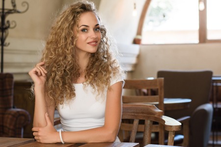 image of young pretty girl sitting at a table with coffee or cappuccino using mobile phone.の写真素材