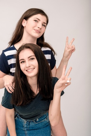 Positive friends portrait of two happy sister girls, funny faces, grimaces, joy, emotions, casual style on light grey backgroundの写真素材