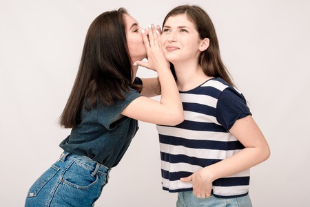 Portrait of a two girls gossip on gray background. Funny faces, grimaces, joy, emotions, casual styleの写真素材