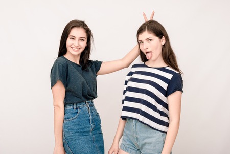 Positive friends portrait of two happy sister girls, funny faces, grimaces, joy, emotions, casual style on light grey backgroundの写真素材