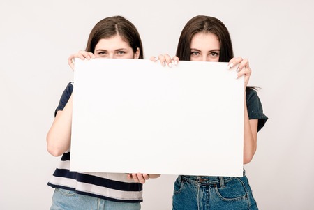 Two happy smiling young business women in casual clothes carrying blank signboard on grey backgroundの写真素材