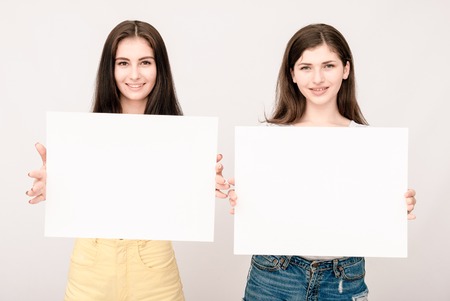 Two happy smiling young business women in casual clothes showing blank signboards on light grey backgroundの写真素材