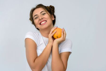 Portrait of young and healthy woman with orange on grey background