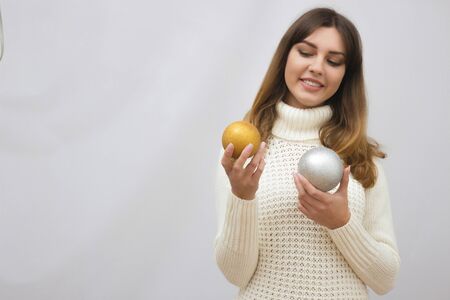 Portrait of a young girl in white sweater with christmas balls in hands, isolated on light grey backgroundの写真素材