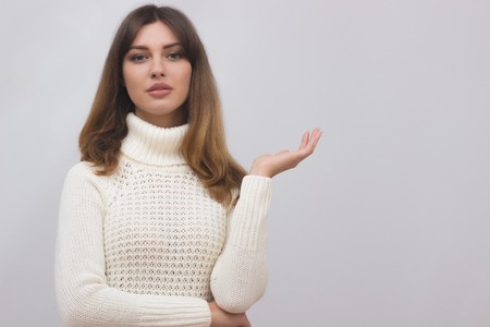 Woman in white sweater showing something with open hand palm. Caucasian female girl presenting something isolated on light grey background. Copyspase for product or sign textの写真素材