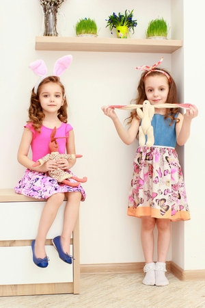 Cute little girls with bunny ears and cuddly toy stand near the white wallの写真素材