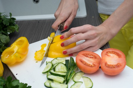 Womans hands cutting tomato, behind fresh vegetables.の写真素材