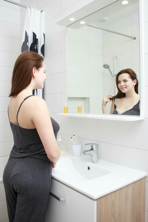morning and people concept - young woman looking to mirror at home bathroomの写真素材