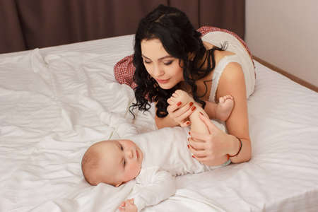 Happy smiling mother and baby lying on bedの写真素材