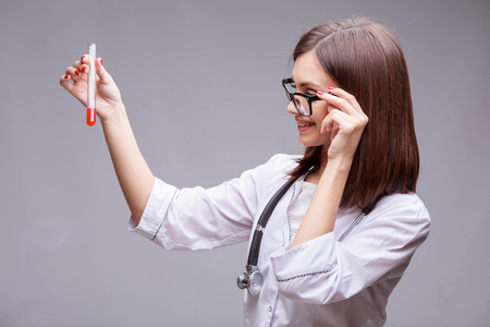 Portrait of an attractive young female doctor or nurse with stethoscope in white uniform holding test tube with blood sampleの写真素材