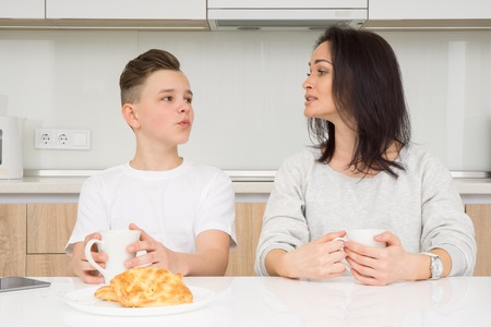 Happy family in the morning. Beautiful woman with her son having breakfast in kitchen together, looking at each otherの写真素材