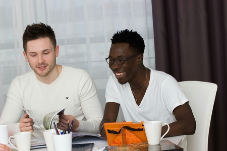 students studing together, students smiling together, students sitting on table, discussing and smiling, international students studing in living roomの写真素材