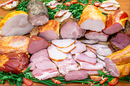 Assortment of meat products including various ham and pork with greens and spices on wooden table closeupの写真素材