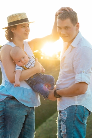Happy family with little baby spending time together at sunset, on summer or autumn day, warm sunlightの写真素材