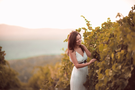 Smiling woman in white dress standing in vineyardの写真素材