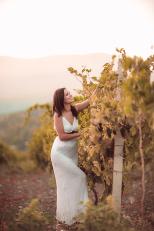 Smiling woman in white dress standing in vineyardの写真素材