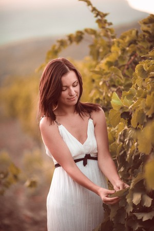 Smiling woman in white dress standing in vineyardの写真素材