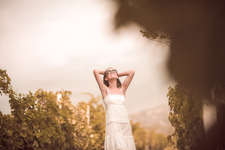 Smiling woman in white dress standing in vineyardの写真素材