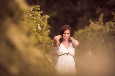 Smiling woman in white dress standing in vineyardの写真素材