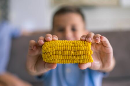 Kid eating cort at home. Boy bite boiled corn in living room