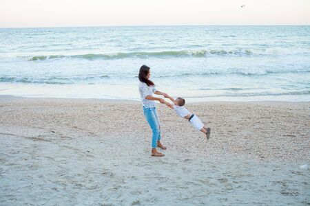 Back view of mother and son playing near sea. Family concept, peaceful scene, wide view of mom and baby running on seashoreの写真素材