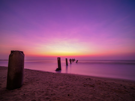 Beautiful sunrise on the beach with old concrete bridge pillars. breakwater in the foregroundの写真素材