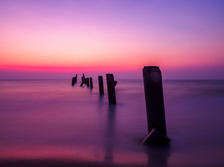Beautiful sunrise on the beach with old concrete bridge pillars. breakwater in the foregroundの写真素材