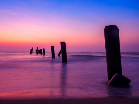 Beautiful sunrise on the beach with old concrete bridge pillars. breakwater in the foregroundの写真素材