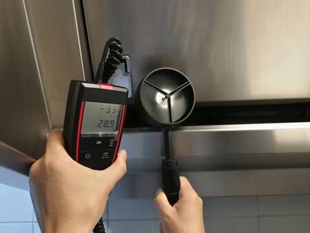 The inspectors are using aneamometer to measure the air velocity of the hood in the kitchen.の写真素材