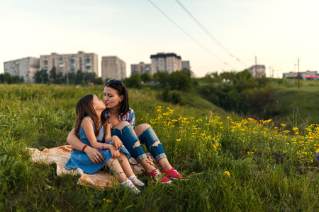 Little cute girl with her mother sitting at sunset in summerの写真素材