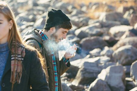 Stylish portrait smoking guy who walks with the girl on the rocky shore of the sea.の写真素材