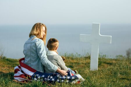 Mom and son are sitting on the grave of a soldier. Mom brought her son to the grave of his father on memorial day 27 mayの写真素材