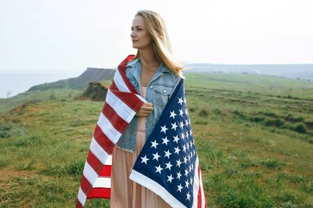 A girl in a coral dress and a denim jacket holds the flag of the united states in her hands. July 4th Independence Day.の写真素材