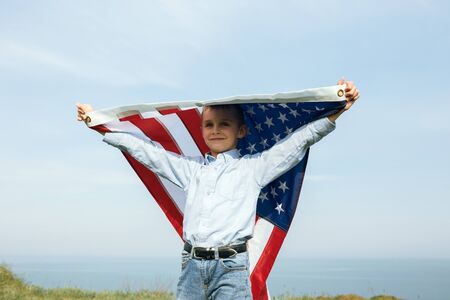 A little boy holds a flag of the United States against the sky. July 4th Independence Day.の写真素材