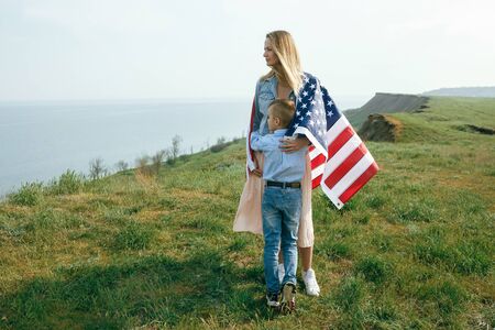 single mother with son on independence day of USA. Woman and her child walk with the USA flag on the...
