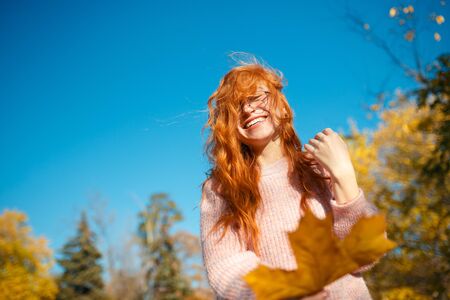 Portraits of a charming red-haired girl with a cute face. Girl posing in autumn park in a sweater and a coral-colored skirt. The girl has a wonderful mood.の写真素材