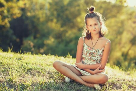 beautiful girl sits on the grass and looks at the camera. Dressed in a sarafanの写真素材