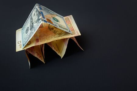 House of bills. The house has a roof of dollar bills. The bills are on a dark table.の写真素材
