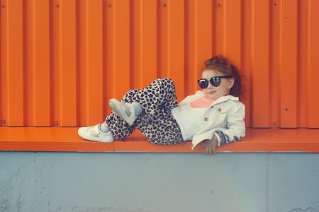 Cheerful mother and daughter having fun in city. Mom and daughter in fashionable clothes are sitting on the street. Wearing leopard pantsの写真素材
