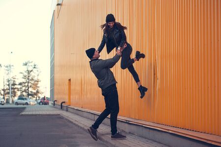 Young couple in love walks by the sity. Spring, autumn. The guy is wearing a jacket and hat. Girl in a hat and leather jacket with a scarfの写真素材