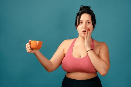 Happy plus size positive woman. Happy body positive concept. I love my body. Attractive overweight woman posing on camera in the studio with tea cup in her hands. Girl is wearing a coral braの写真素材