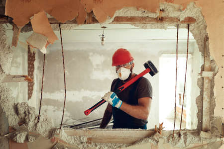 builder with perforator drills holes in concrete wall The builder is dressed in a protective suit...