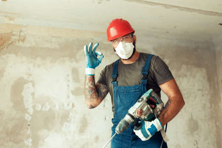 builder with perforator drills holes in concrete wall The builder is dressed in a protective suit...