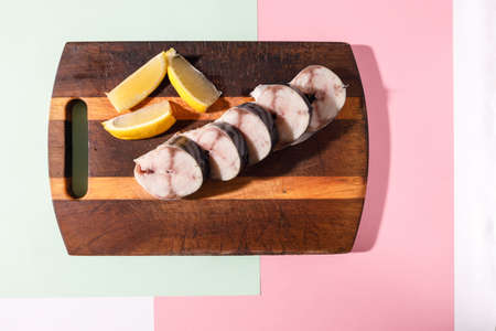 Fresh mackerel cut into pieces lies on a kitchen board with lime on a bright colored background