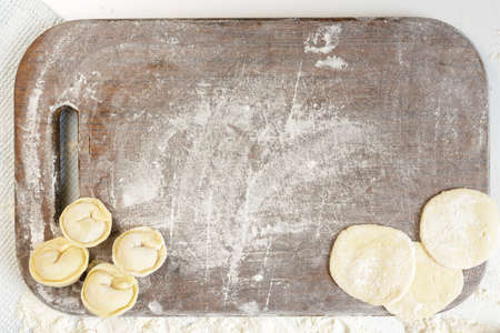 homemade dumplings in the kitchen without decorations. kitchen board sprinkled with flour with dumplings and dumplings doughの写真素材